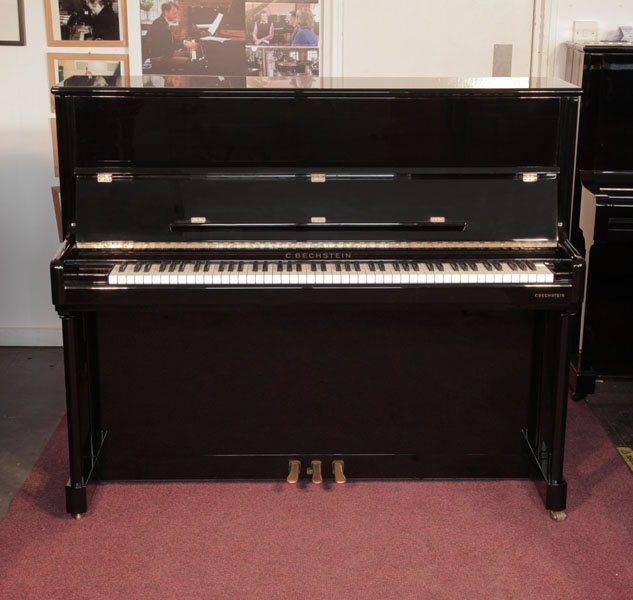 A 2001, Bechstein  Elegance124 upright piano for sale with a black case and brass fittings. Piano has an eighty-eight note keyboard and three pedals. 