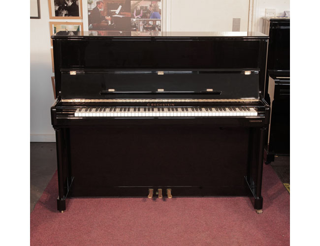 A 2001, Bechstein Elegance 124 upright piano for sale with a black case and brass fittings. Piano has an eighty-eight note keyboard and three pedals.