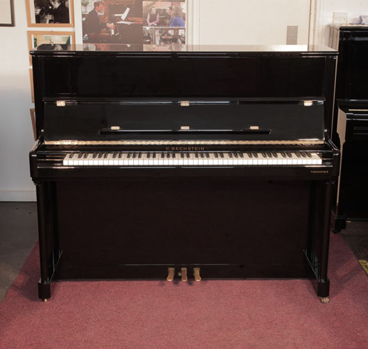 A 2001, Bechstein Elegance 124 upright piano for sale with a black case and brass fittings. Piano has an eighty-eight note keyboard and three pedals. 