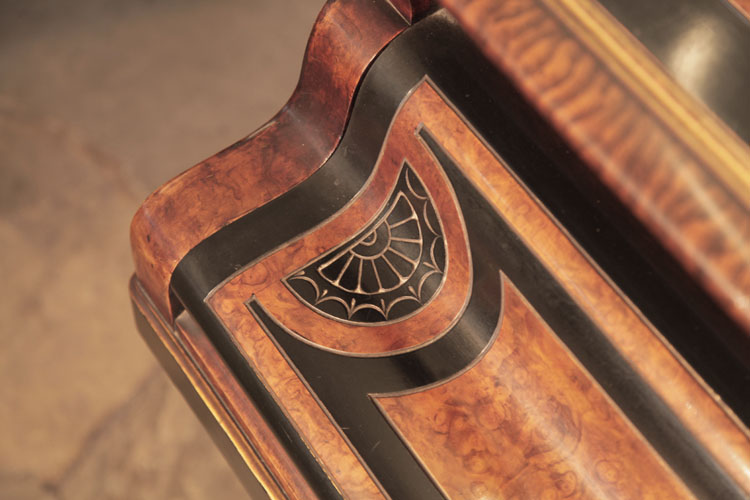 The piano fall repeats smaller versions of the decorative carvings seen on the lid. A semi-circular motif in black and walnut contains a sun motif is bordered with stylised swags and palm leaves 