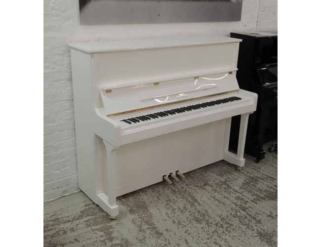 A brand new, Feurich Model 122 upright piano in white gloss with brass fittings. Piano has an eighty-eight note keyboard and three pedals.